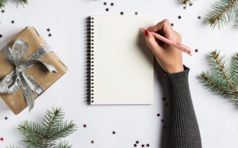 Notebook on a table with a right arm holding a pencil writing a list