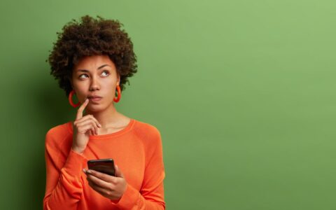 Woman in orange looking curious while ohlding her phone