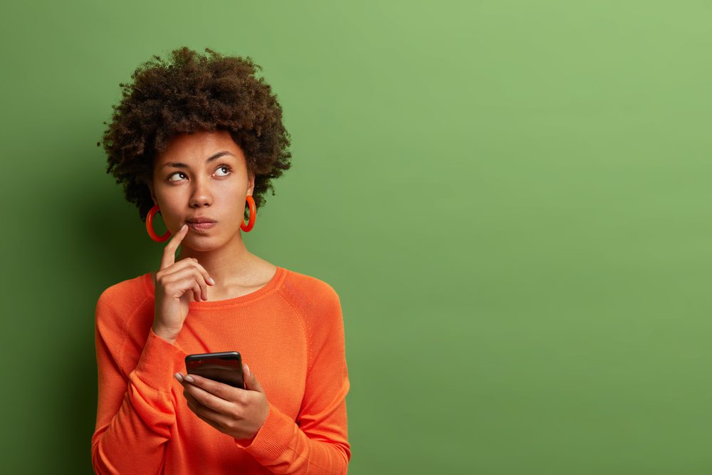 Woman in orange looking curious while ohlding her phone